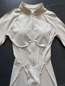 Détail d'un body de sport beige avec coutures structurées et demi-fermeture éclair