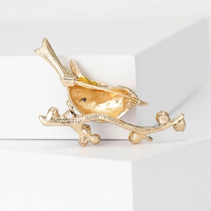 Broche élégante pie dorée sur branche avec finition mate sur socle blanc moderne