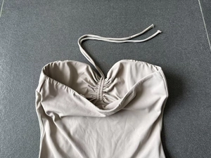 Détail de haut yoga beige avec cordon de serrage et licou sur fond gris texturé