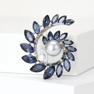 Dettaglio della spilla a spirale con cristalli blu scuro e perla grigia su sfondo bianco