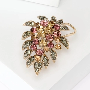 Détail d'une élégante broche raisin dorée avec strass roses et champagne sur bloc blanc