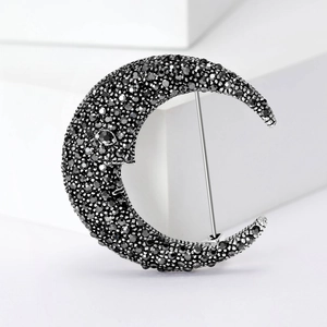Silver crescent moon brooch with black crystals on a white geometric display stand