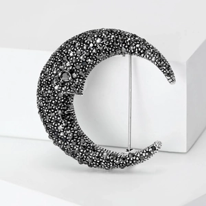 Detailed close-up of crescent moon brooch with black rhinestones on a silver base