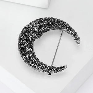 Detailed close-up of a crescent moon brooch with black rhinestones on silver metal base