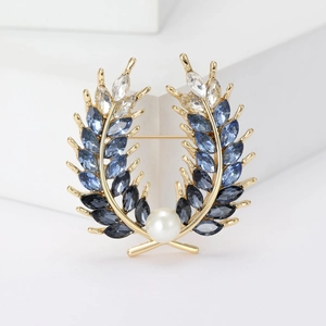 Détail macro d'une broche en forme de blé avec cristaux bleu-gris et perle blanche