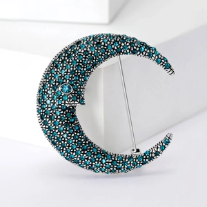 Macro shot of silver moon brooch with blue rhinestones on white geometric background