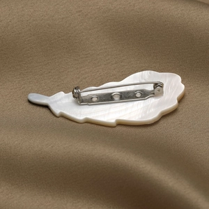 Broche plume élégante avec incrustation en nacre sur fond de tissu en soie luxueux