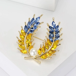 Détail d'une broche en blé doré avec cristaux bleus et jaunes et perle blanche