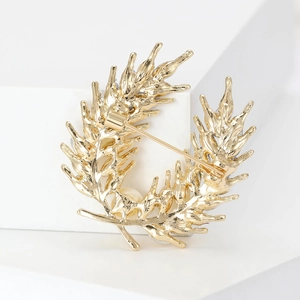 Élégante broche couronne de blé dorée avec détail de l'épingle sur socle blanc