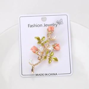 Gros plan d'une broche rose dorée avec des accents de perles et feuilles vertes