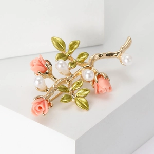 Détail d'une élégante broche branche dorée avec roses roses, feuilles émaillées et perles
