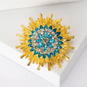 Vintage gold sunburst brooch with blue sapphire crystals on a white pedestal