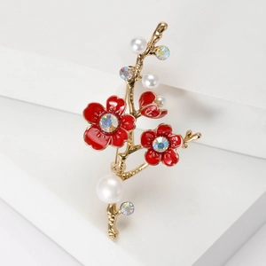 Élégante broche fleur de prunier dorée avec émail rouge, perles et cristaux sur fond blanc