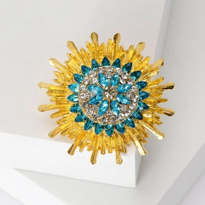 Elegant gold-trimmed sunflower brooch with blue and white rhinestones on geometric display