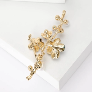 Vue détaillée d'une broche branche de prunier dorée avec des perles blanches fines
