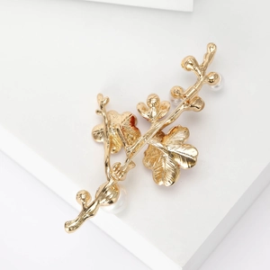 Élégante broche branche de prunier dorée avec perles sur un socle blanc épuré