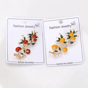 Detail of red and yellow persimmon brooches with enamel glaze and green leaves