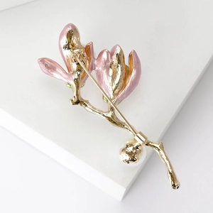 Elegant magnolia flower brooch with pink enamel petals and gold finish on a white pedestal