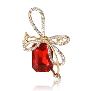 Elegant gold bow brooch with red crystal gemstone and white rhinestones on white background