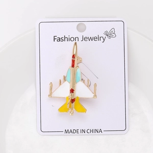 Detail view of colorful enamel fighter jet brooch with gold metal frame on a white card
