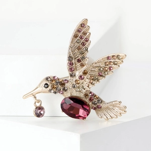 Détail macro de broche colibri avec pierre violette et strass colorés sur métal doré