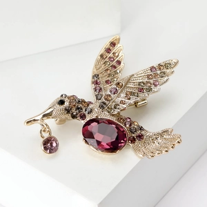 Élégante broche colibri dorée avec cristal violet et strass sur des marches blanches