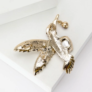 Broche colibri dorée élégante avec fermoir épingle et pendentif cloche sur socle blanc