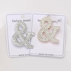 Vista dettagliata delle spille a forma di ampersand argento e oro con strass lucidi