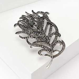 Detail view of vintage peacock feather brooch with grey rhinestones on a white pedestal