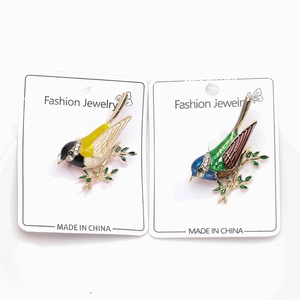 Vue détaillée de deux broches oiseaux en émail coloré avec strass sur des branches dorées