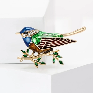 Détail macro de broche martin-pêcheur avec émail coloré, strass et branche d'oiseau dorée