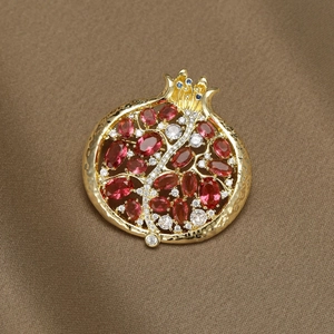 Elegante broche de granada dorada con circonitas rojas y cristales sobre fondo de seda