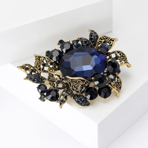 Detailed close-up of vintage gold brooch with large blue oval gemstone and dark crystals