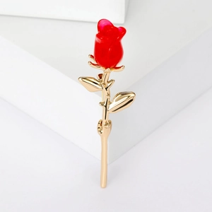Macro détaillée d'une broche rose en émail rouge avec tige dorée sur fond blanc