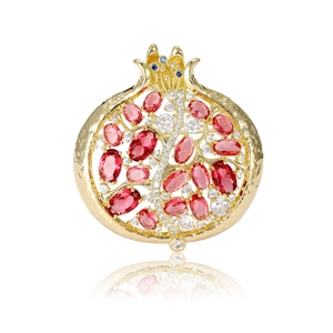 Elegante broche granada con piedras rojas y baño de oro sobre fondo blanco puro