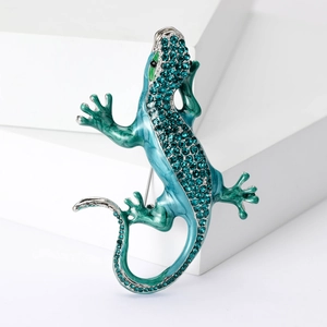 Macro shot of green enamel lizard brooch with blue rhinestones on a white geometric base