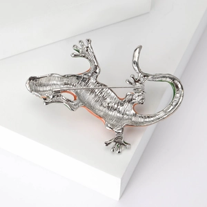 Back view of silver lizard brooch with orange enamel accents on a white display stand