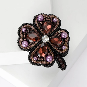 Détail de la broche trèfle avec pierres bordeaux et accents de perles violettes
