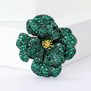 Detail of green zircon camellia brooch with gold stamens on a white pedestal