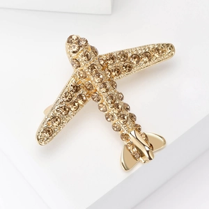 Détail macro d'une broche avion dorée ornée de strass champagne sur décor blanc