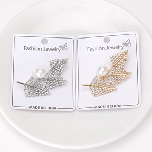 Close-up of leaf-shaped pearl brooches in gold and silver with sparkling rhinestones