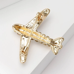 Broche avion dorée élégante avec strass pour costume sur un piédestal blanc épuré