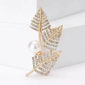 Elegant gold leaf brooch featuring white rhinestones and a large pearl on a white pedestal