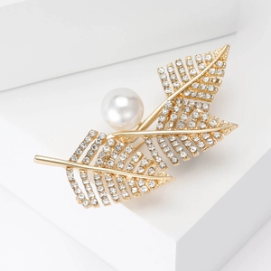 Detailed view of the golden leaf brooch featuring sparkling crystals and a large white pearl
