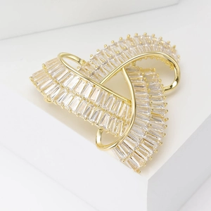 Détail d'une broche géométrique de luxe dorée avec zircons baguette sur support blanc