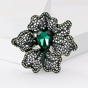 Detail of hollow black metal flower brooch with emerald green pear-cut crystal inlay