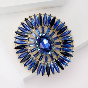 Macro view of luxury gold-tone brooch featuring a large oval blue crystal and rhinestones
