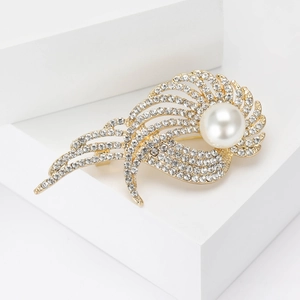 Dettaglio dell'elegante spilla a piuma dorata con strass scintillanti e perla bianca