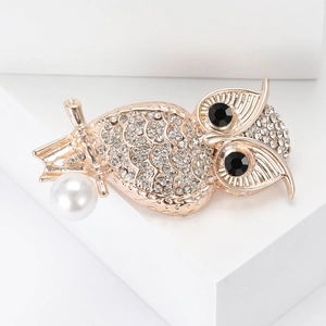Vue détaillée de la broche hibou de luxe avec strass blancs et une perle blanche suspendue