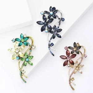 Détails de trois broches en forme de fleurs ornées de strass colorés et cristaux fins